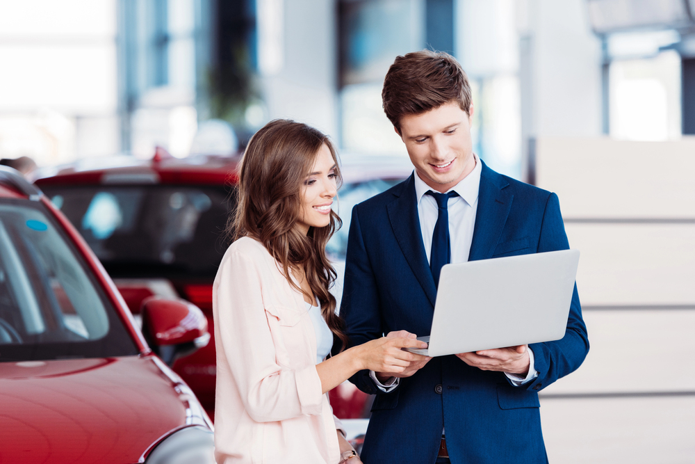 Vrouw kijkt mee op laptop van auto verkoper